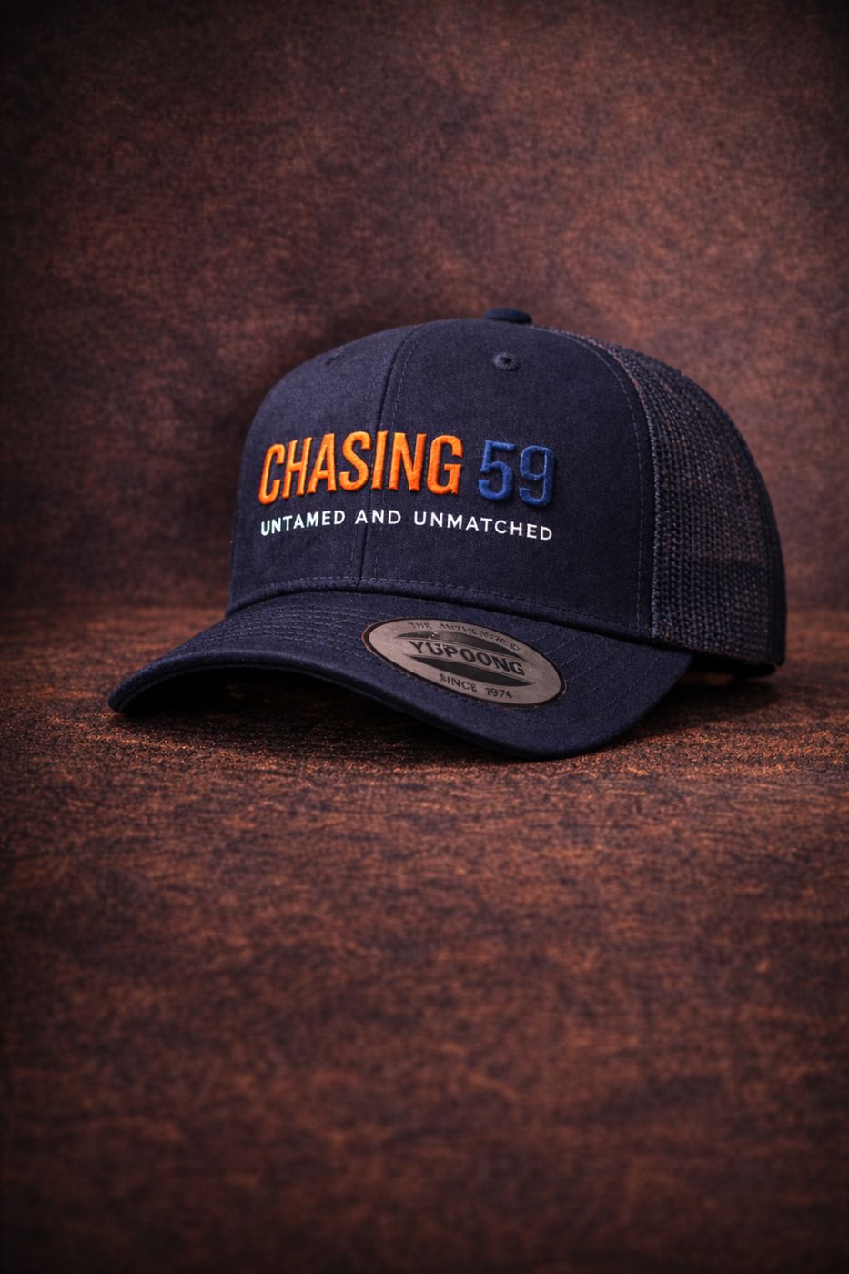 Design render of the navy CHASING 59 trucker cap with orange embroidery